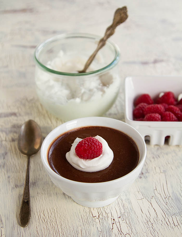 Chocolate Pot de Creme topped with coconut whipped cream and fresh raspberries